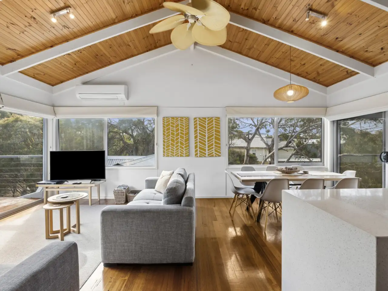 Open-plan living room with timber ceiling, grey sofas and the dining table beyond